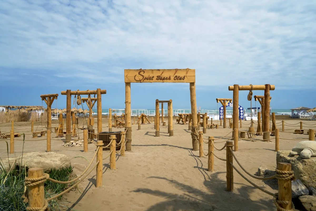Wooden outdoor fitness equipment on the sand by the Sport Beach Club arch